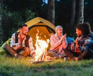 Group of friends enjoying a campfire in front of a tent at night