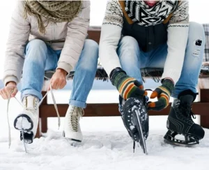 Two people tying ice skates on a snowy bench, showcasing high-quality ice skate rentals available nationwide.