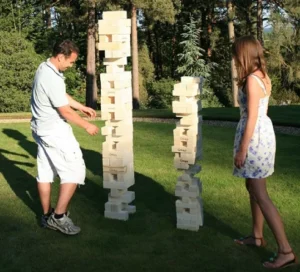 Two people playing a giant Jenga game outdoors on a sunny day, available for rent at North Sport Rentals