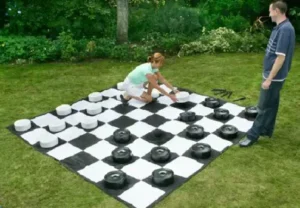 Two people setting up a giant checkers game on a lawn, available for rent at North Sport Rentals