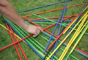 A hand picking up colorful giant pick-up sticks on a lawn, available at North Sport Rentals