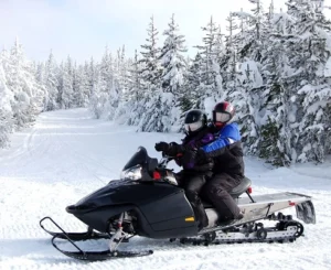 Two snowmobilers enjoying a winter ride through a scenic snowy forest trail. North Sport Rentals 