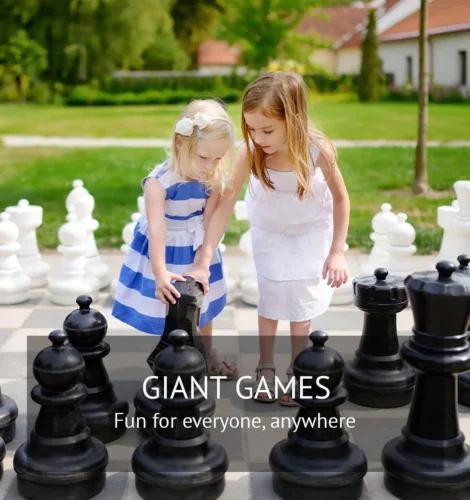 Two young girls playing with oversized chess pieces in an outdoor park setting.