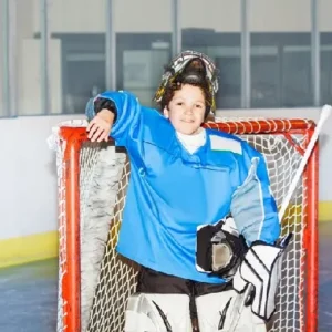 Young ice hockey goalie leaning on the net in full gear in Minneapolis