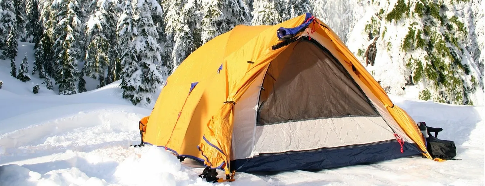 Winter camping setup with a bright orange tent in the snow, showcasing North Sport Rentals' corporate winter camping rentals for team-building events.