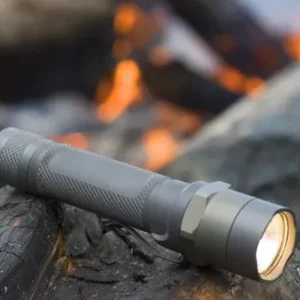 High-quality flashlight resting on a log with a campfire glowing in the background, perfect for outdoor adventures