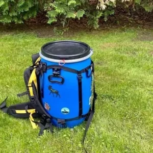 Blue bear-resistant food container with a backpack harness sitting on green grass.