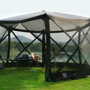 Woman relaxing on a cot inside a screened outdoor canopy tent by a lake.