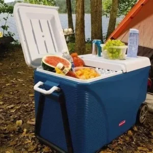 Large blue cooler filled with food and drinks at a campsite near a lake.