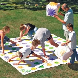 A group of people playing a jumbo outdoor twister game on a large mat with colorful spots in a sunny park.