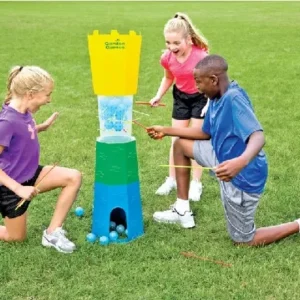 Three children playing a giant Cannonball Drop game on a grassy lawn, carefully pulling out sticks while balancing blue balls.