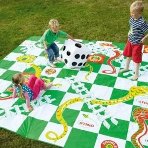 Three kids playing a giant Snakes and Ladders game on a sunny lawn with a large dice.