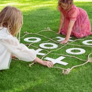 Two young girls playing a giant tic-tac-toe game on a rope grid laid out on a grassy lawn.