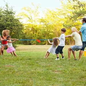 Two families playing tug of war outdoors, with parents and children pulling the rope on opposite sides.