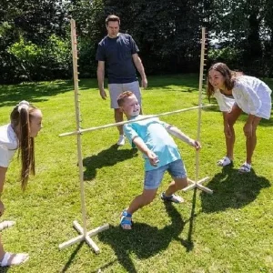 A young boy leaning back to pass under a limbo stick, surrounded by family members cheering him on in a backyard setting.