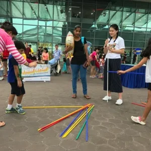 A group of children and adults participating in a giant pick-up sticks game at an outdoor community event.