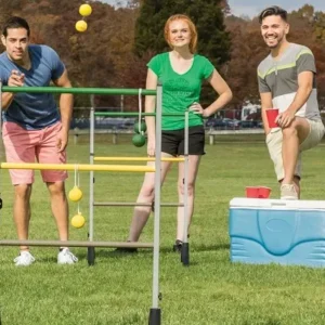 Three adults playing a ladder toss game at a park, with colorful bolas and a cooler nearby for refreshments.