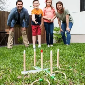 A family of four playing a ring toss game outdoors, taking turns tossing rings at pegs in a backyard.