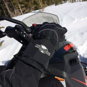 Close-up of a snowmobiler wearing black gloves, gripping handlebars on a snowy trail.