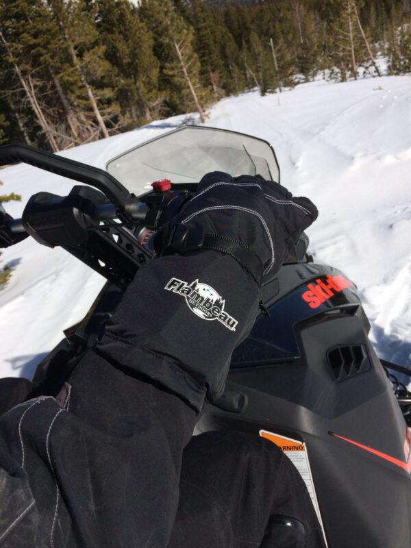 Close-up of a snowmobiler wearing black gloves, gripping handlebars on a snowy trail.