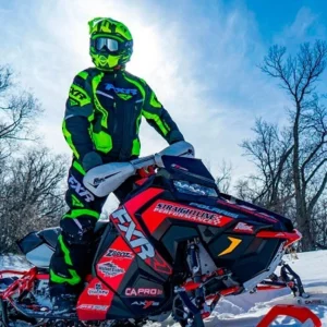 Snowmobiler in neon green gear standing on a snowmobile under a bright blue sky