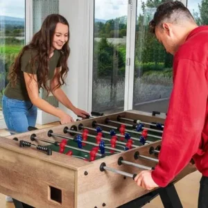 A young woman and a man enjoying a game of foosball in a bright room with large windows overlooking a scenic view.