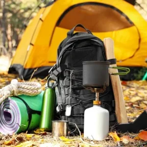 A set of camping essentials, including a backpack, cooking gear, rope, and a tent, arranged outdoors with autumn leaves in the background.