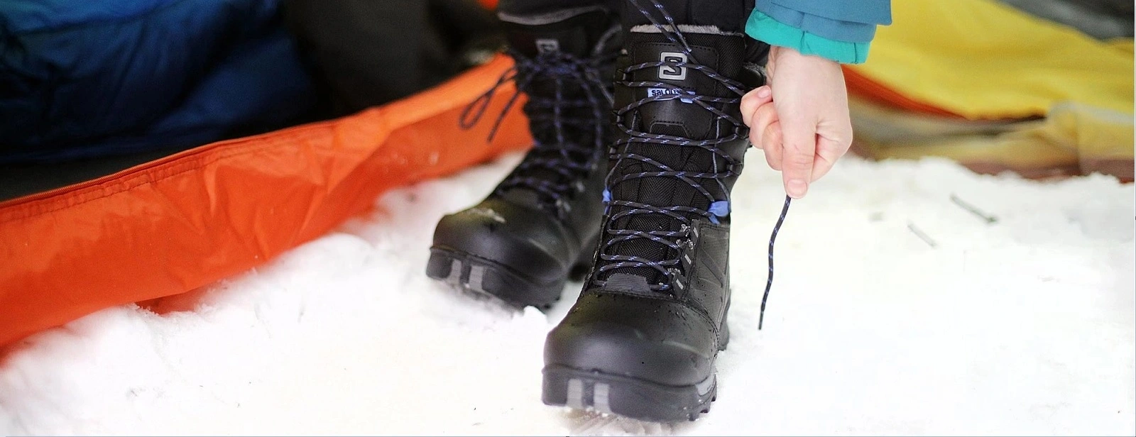 Winter Boots in the Snow - North Sport Rentals Person tying laces on black Salomon winter boots in the snow near an orange tent. Winter boots for rent in Minnesota