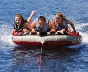 Three friends on a red and black towable tube, laughing as they glide across the open water.