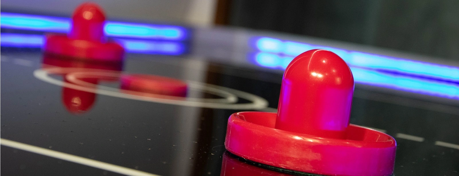 Air hockey rentals in Minneapolis is featuring a close-up of a red mallet on a sleek air hockey table.