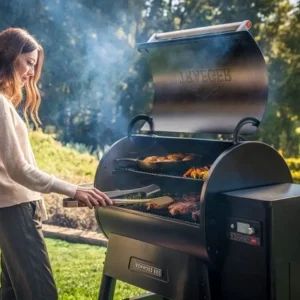 A woman grilling vegetables and meat on a modern digital pellet smoker in a sunny backyard.