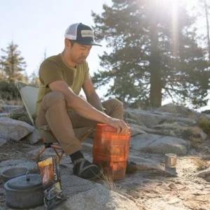 Person sitting near camp with a bear canister in the wilderness