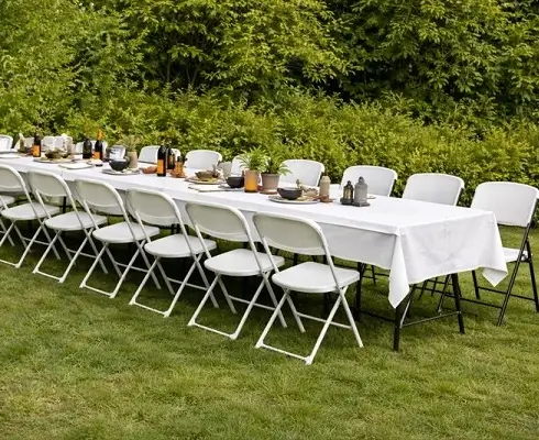 Long white banquet table with folding chairs set up outdoors for an event